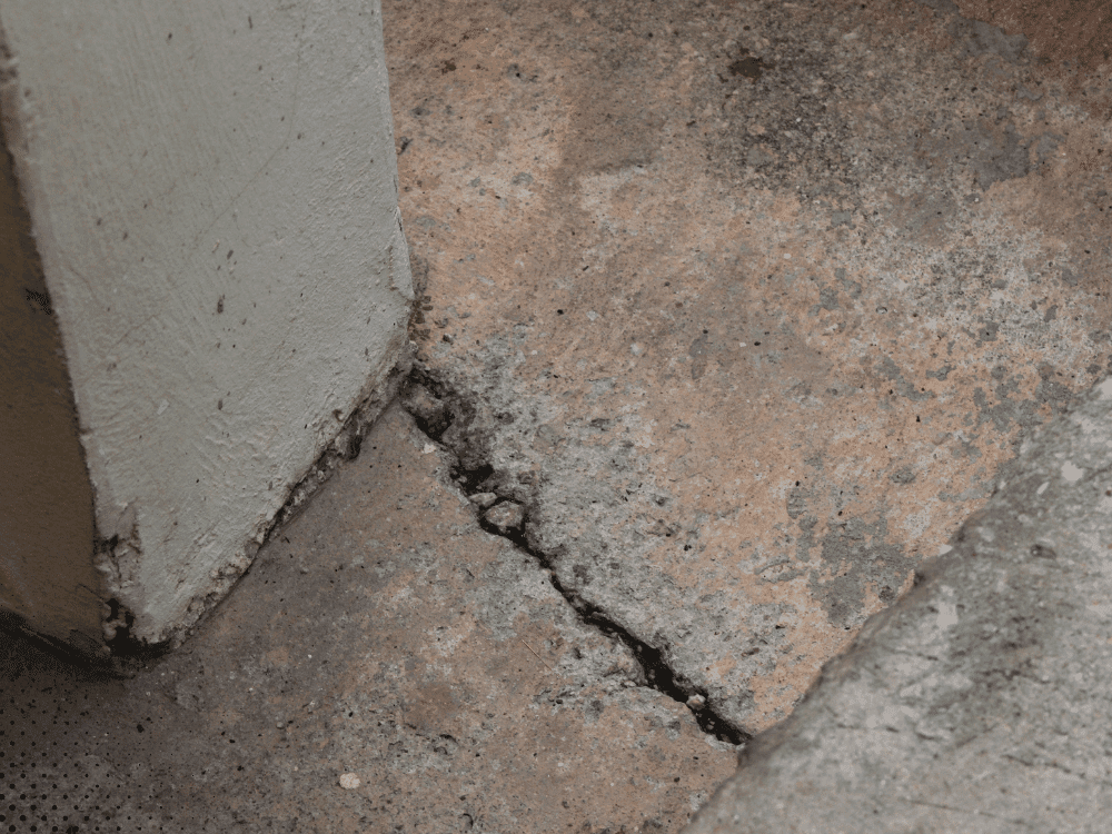 Concrete slab crack near foundation corner indicating possible settlement or soil movement damage